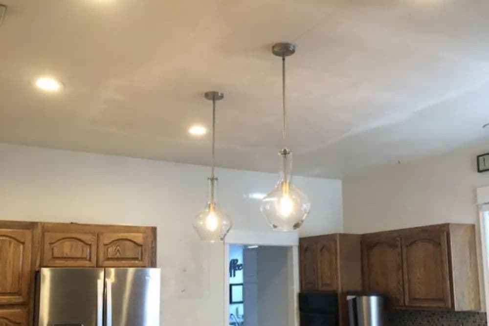 Modern kitchen featuring wooden cabinets, stainless steel fridge, and stylish pendant lighting.
